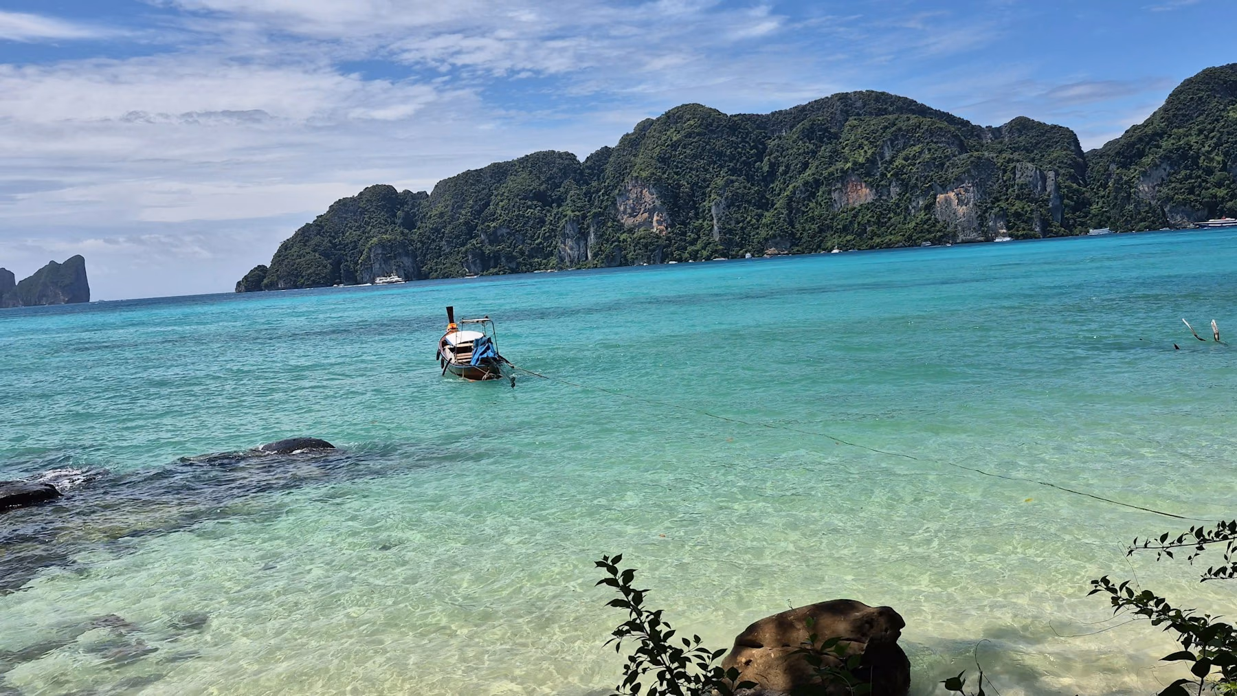 A long-tail boat in clear turquoise water below green limestone cliffs in Thailand